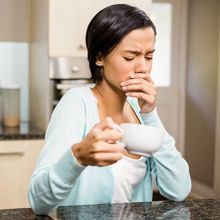 woman holding coffee cup covering mouth