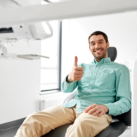 Hombre sonriendo en el sillón dental con el pulgar hacia arriba