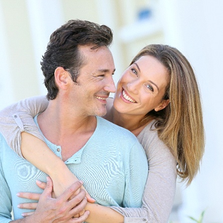 A middle-aged couple smiles while hugging each other, pleased with the result of their metal-free crowns