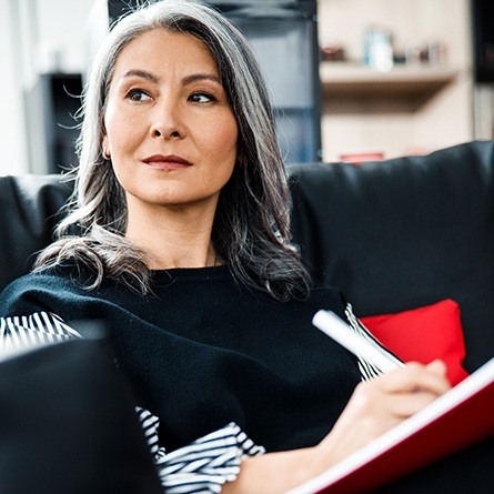 woman sitting on couch righting on notebook