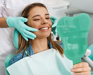 woman smiling while looking in dental mirror 