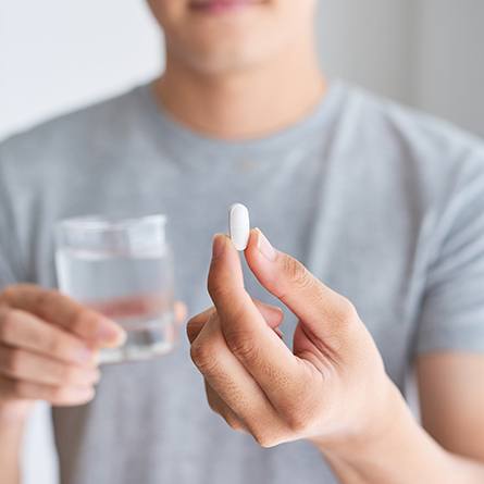 man holding pill and glass of water