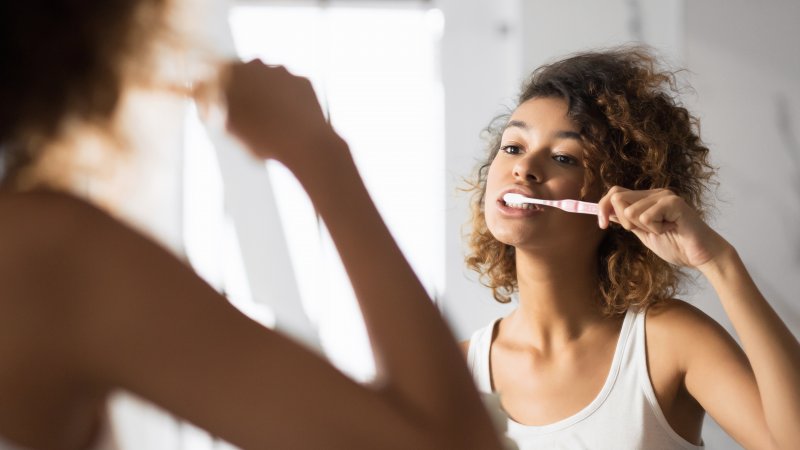 a young woman with dark hair standing in front of the bathroom mirror brushing her teeth