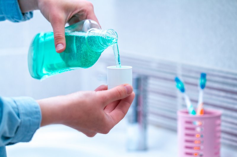 a person pouring mouthwash into a cup in preparation for rinsing 