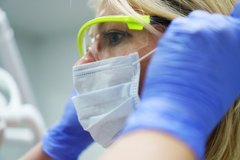 a female dentist wearing gloves, a face mask, and protective eyewear before a patient arrives