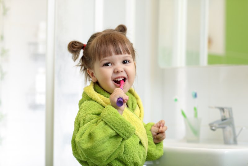 a little girl wearing a green robe and brushing her teeth in the bathroom