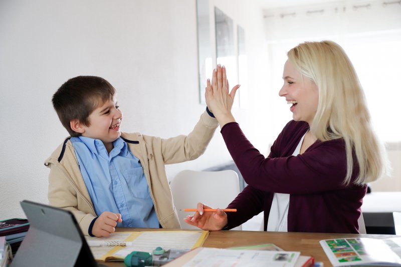 a mother and son high-five while completing schoolwork at home